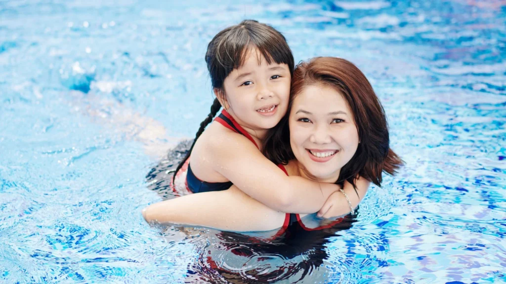 Ibu mendampingi anak yang takut berenang di kolam dalam.